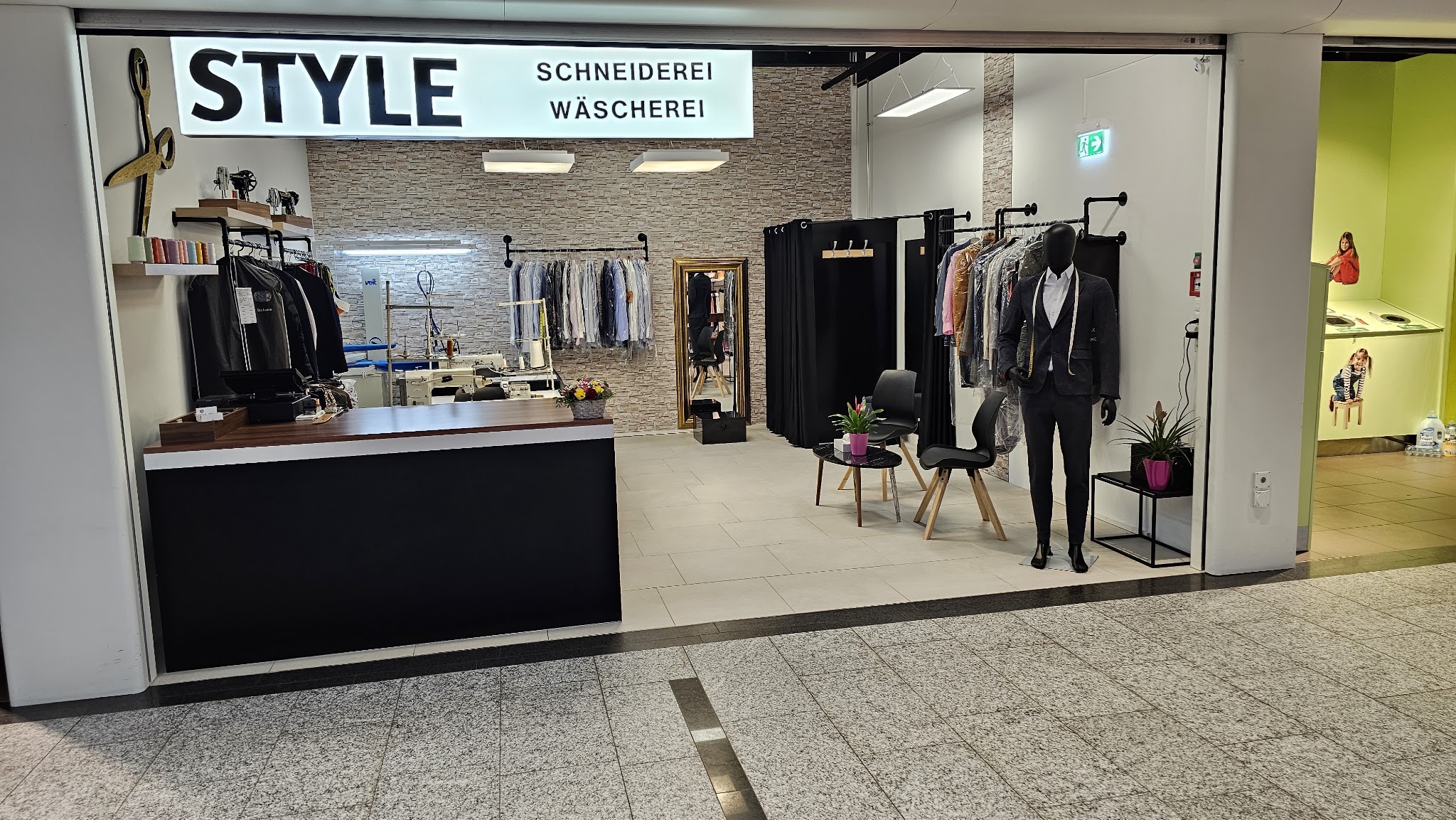 Der Eingang der Style Schneiderei im Zentrum Regensdorf mit Leuchtschrift und Anzug auf der Schneiderpuppe