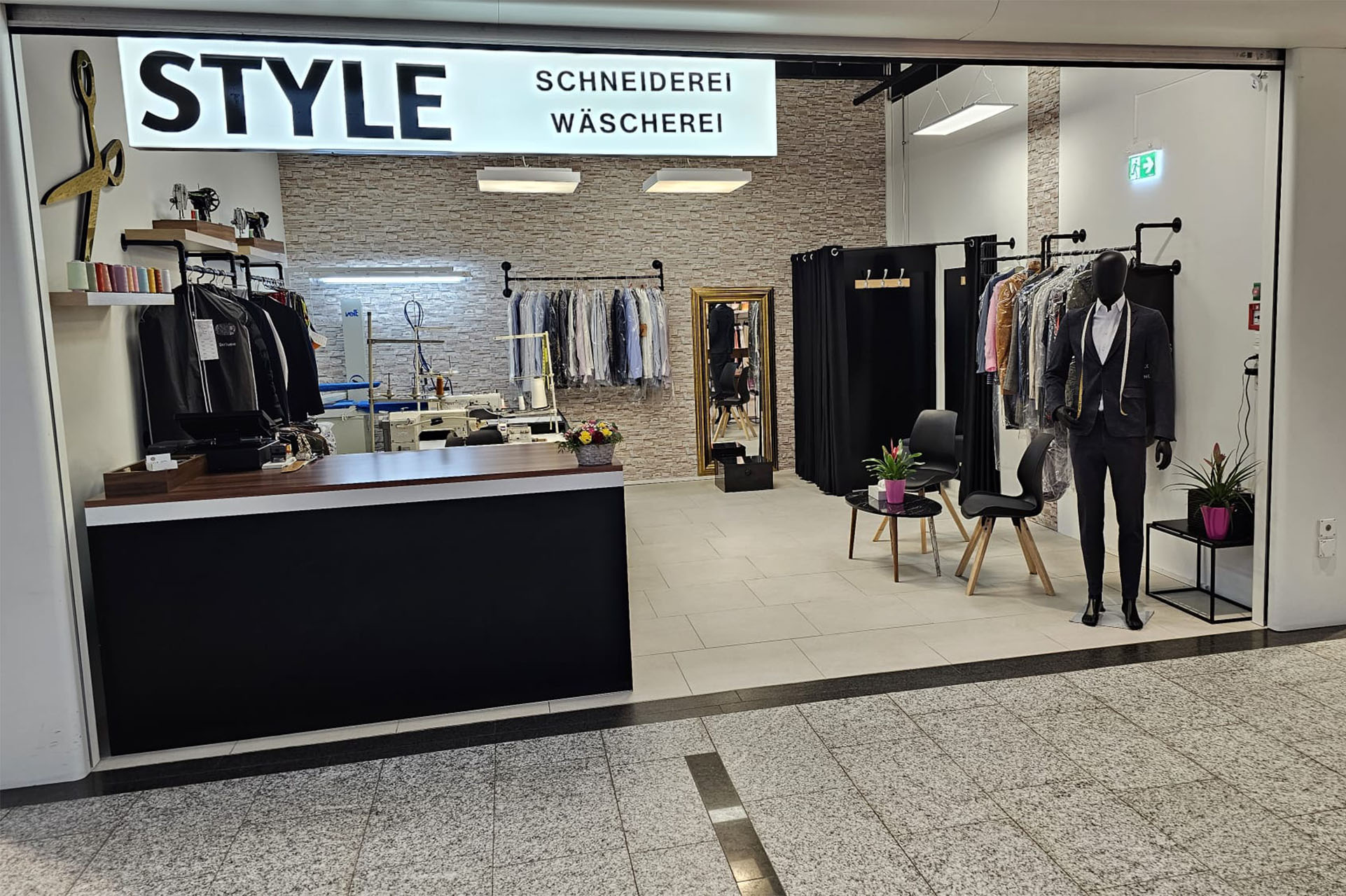 Das Atelier der Style Schneiderei mit Leuchtschrift, Theke, Nähmaschinen und Anzug auf der Schneiderpuppe